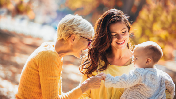 Grandmother and mother smiling at baby in autumn park
