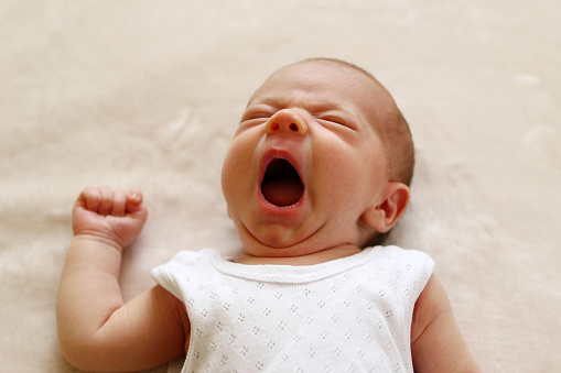 One month child is yawning lying on a blanket