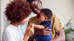 Loving Parents Playing With Newborn Baby At Home In Loft Apartment