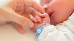 Newborn baby boy sleeping in his crib, his mother's hand holding his little hand.