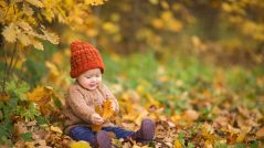 baby in knitted hat and jacket sits on grass in park