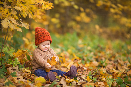 baby in knitted hat and jacket sits on grass in park